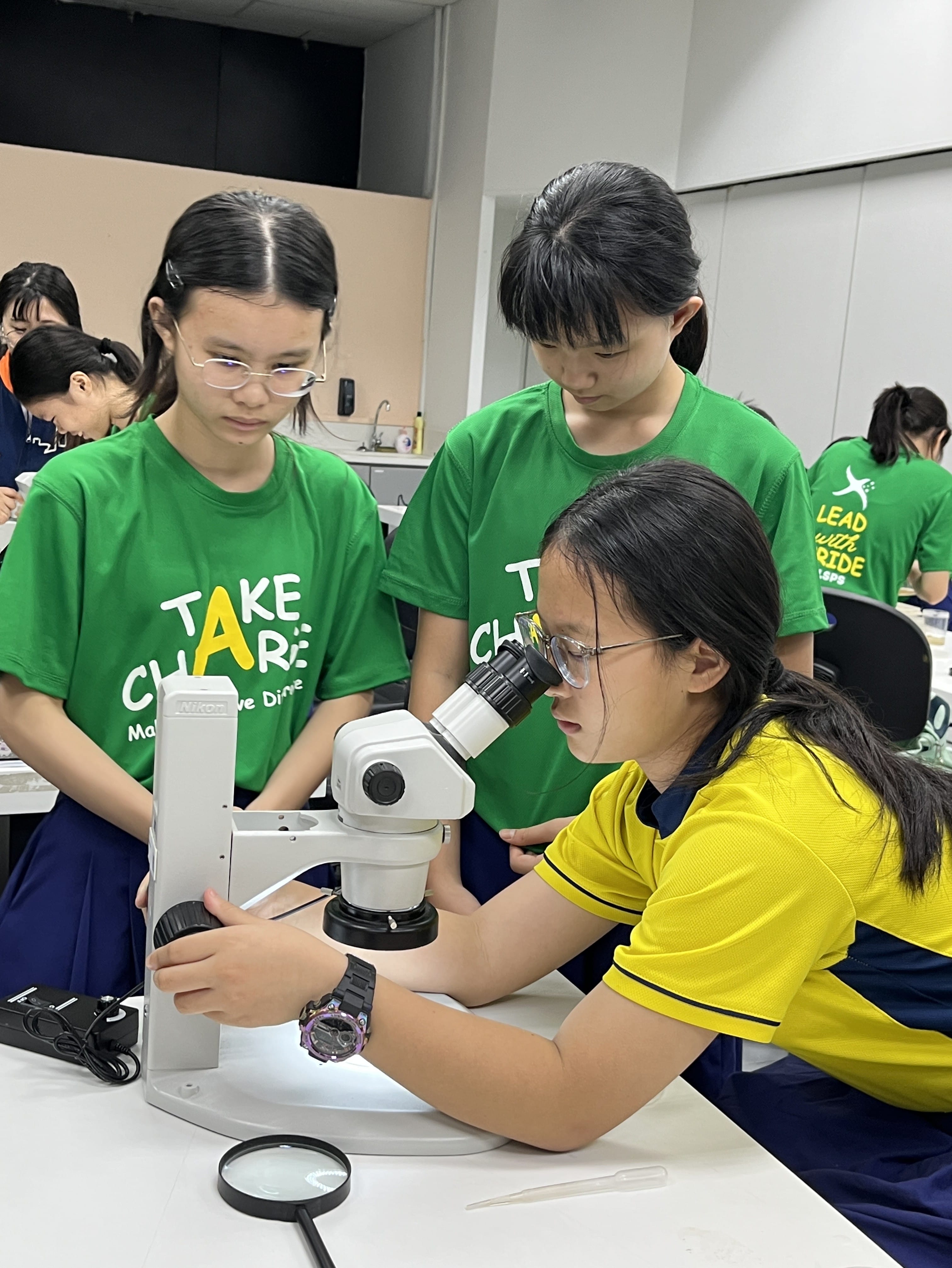 A student adjusting the focus on the microscope as two classmates help from the sides